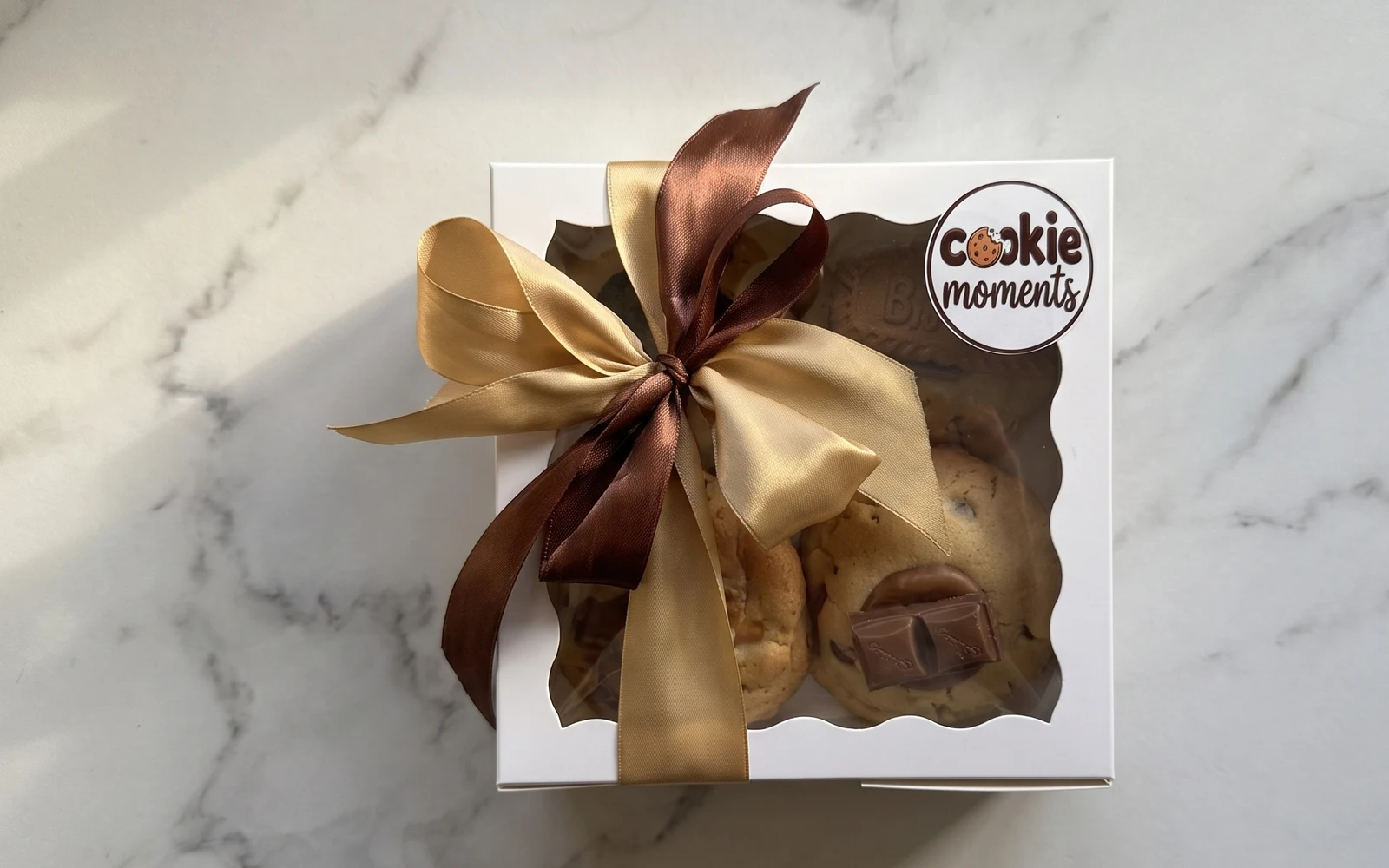 A Cookie Moments box of four on a white marble bench, tied with brown and gold ribbon