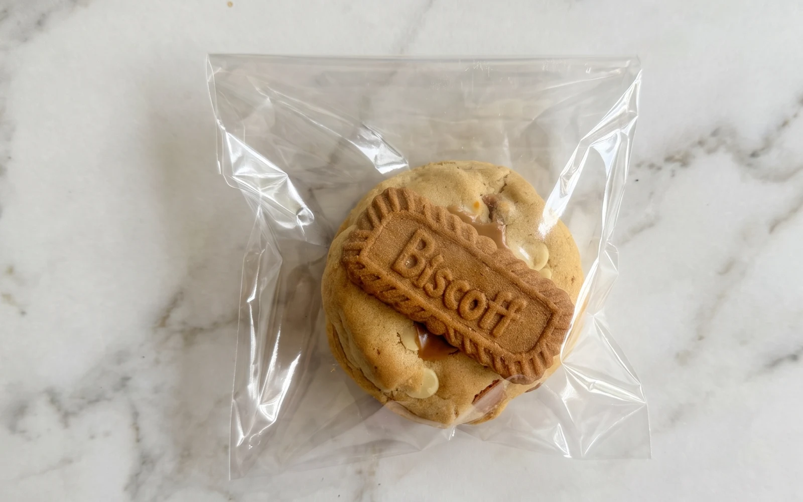 A single Biscoff loaded cookie, wrapped and sealed, on a white marble bench
