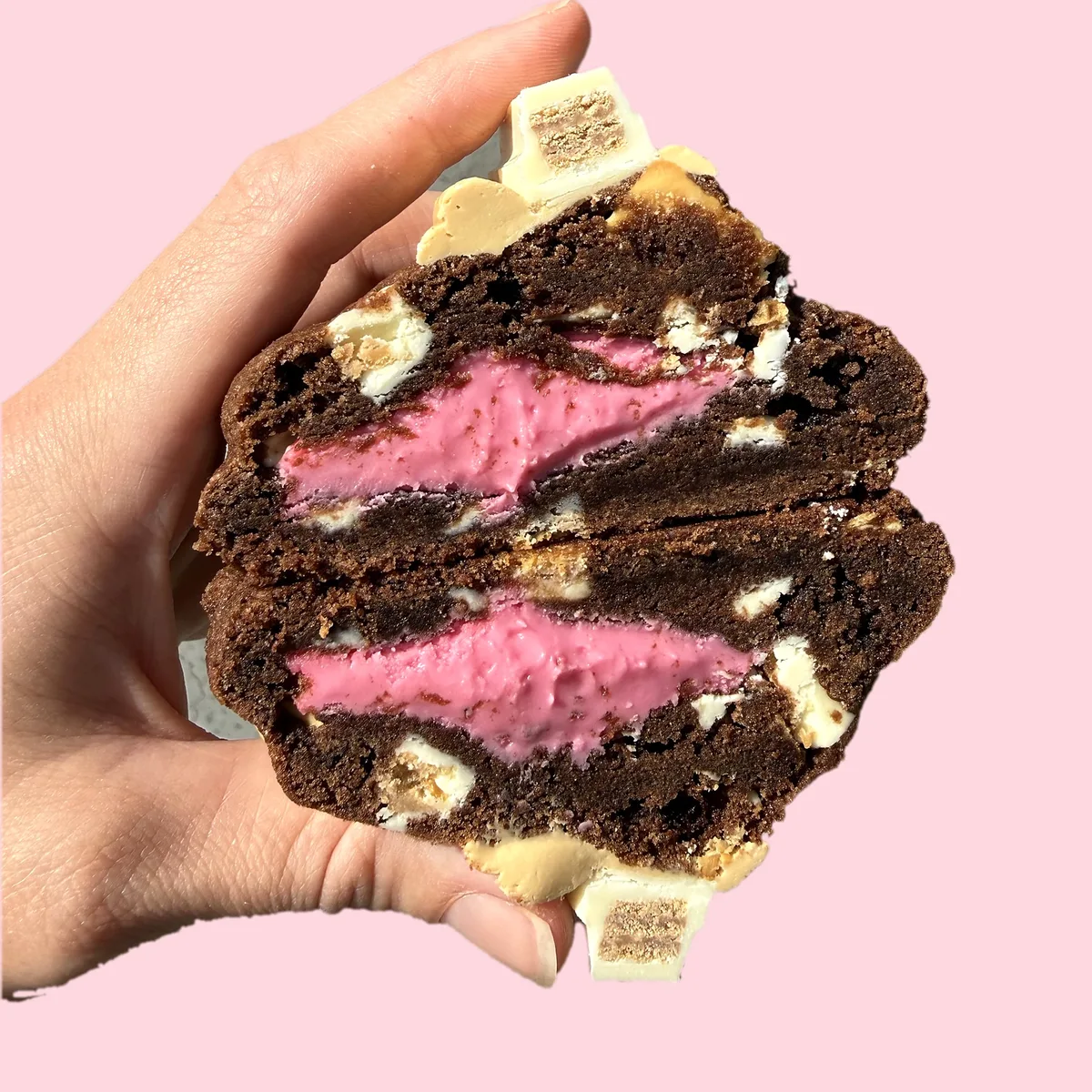 Milky Way KitKat cookie cut in half, showing a strawberry spread centre and white KitKat pieces in double chocolate cookie dough