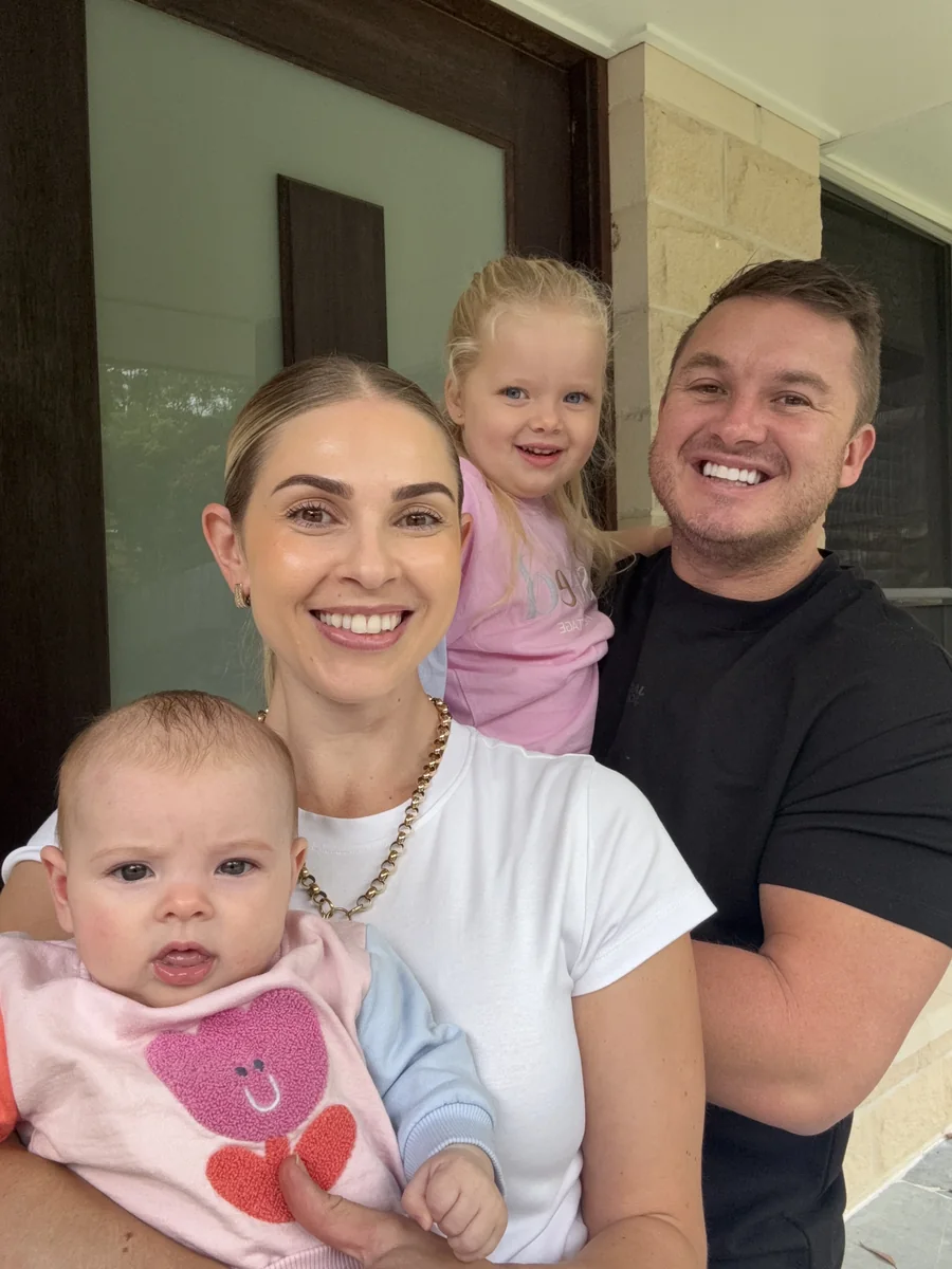Ashley with her partner and their two young daughters at the front door of the family home